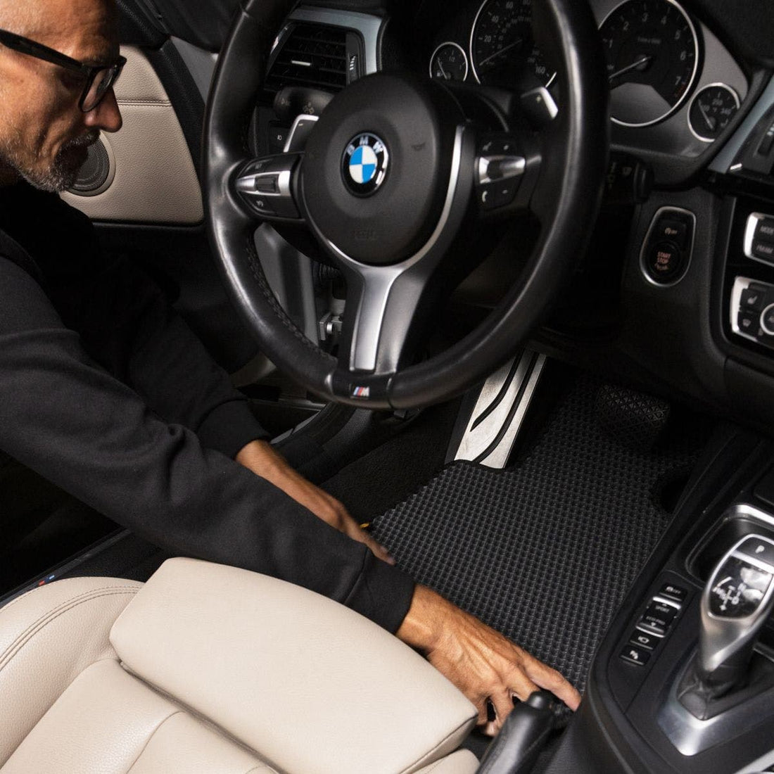 Kierowca montuje wykladzyne EVA w wnetrzu BMW z czarno-bezowym wykonczeniem.