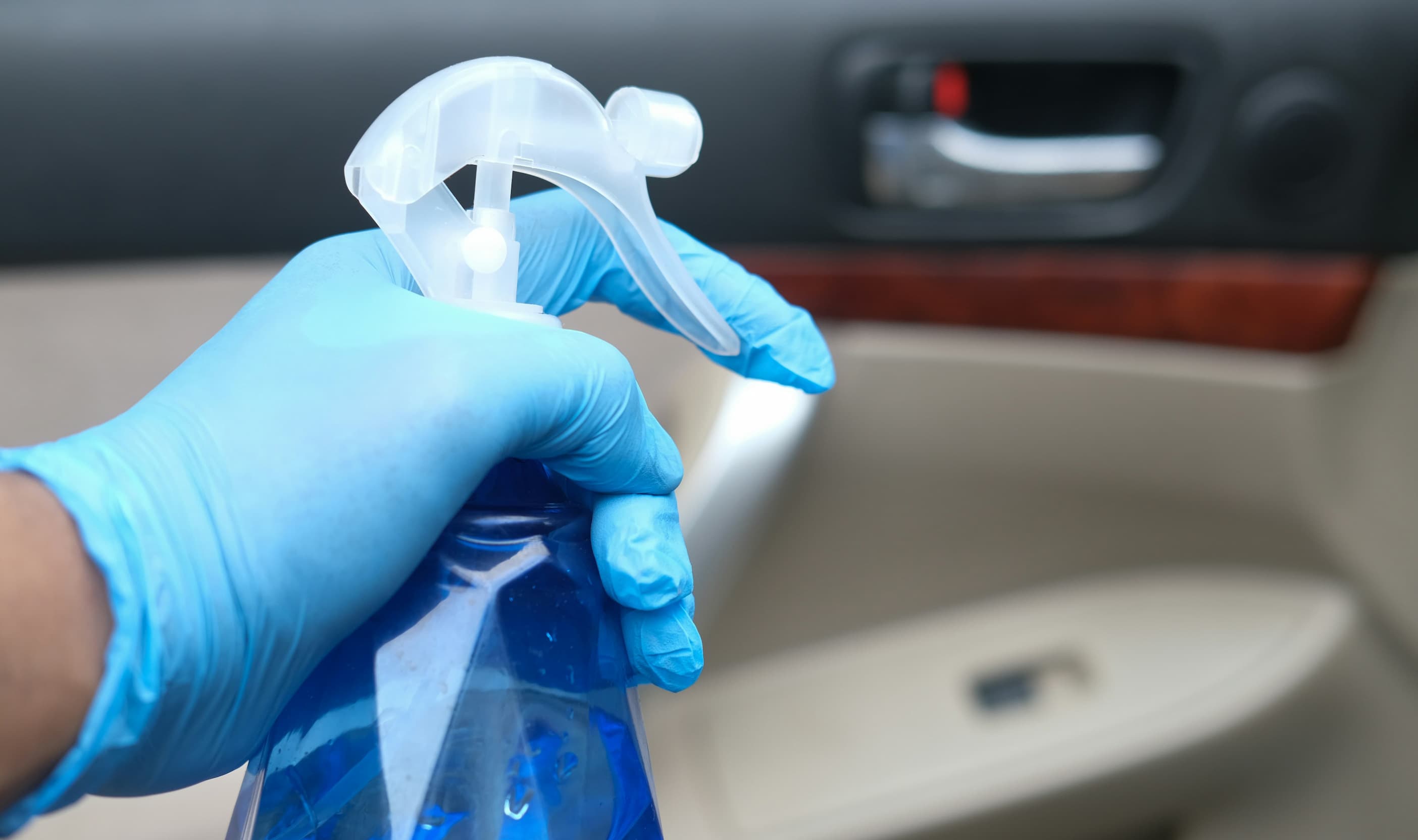 Czyszczenie wnętrza drzwi samochodu sprayem dezynfekującym w rękawicach.