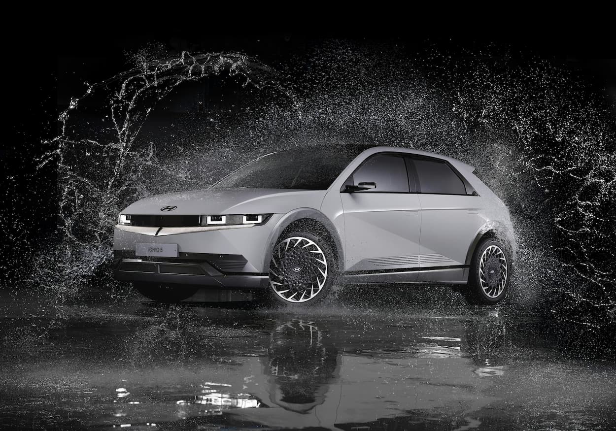 Elektryczny samochod jedzie nocą przez duzy rozprysk wody, pokazujac dynamiczny ruch na mokrej nawierzchni.