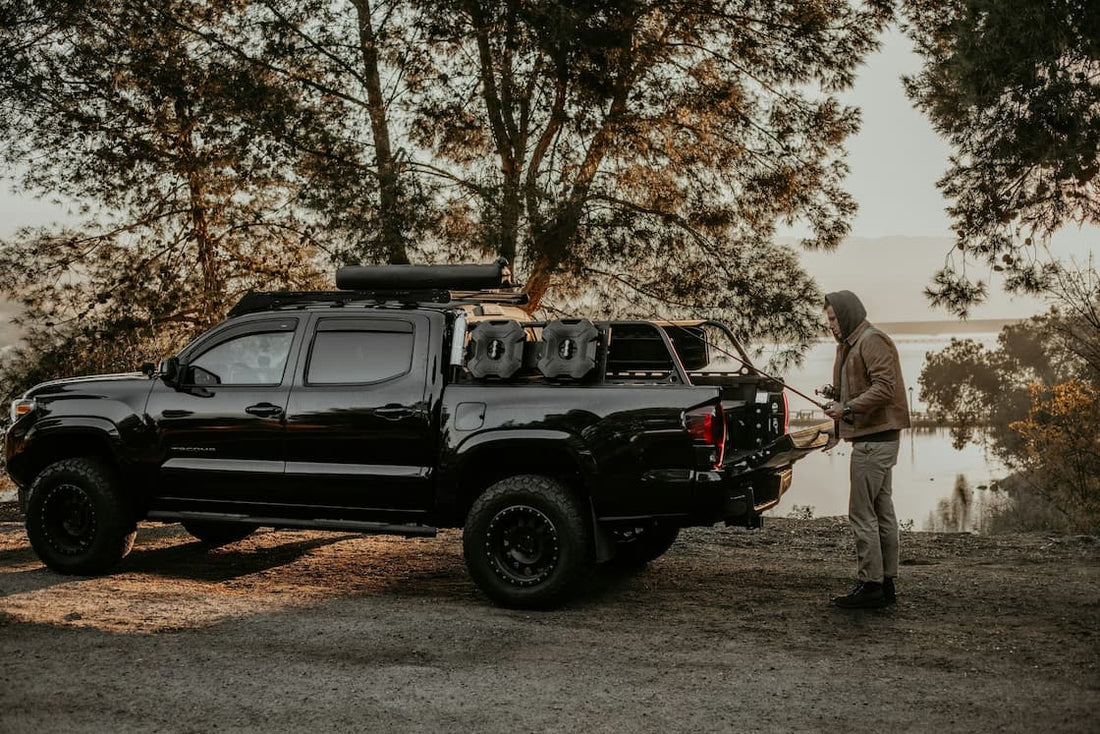 Pickup przygotowany do overlandingu nad jeziorem, mężczyzna układa sprzęt kempingowy.