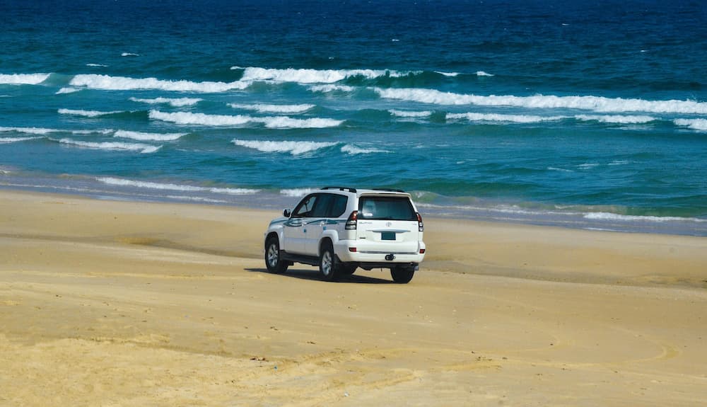 SUV jadący po piaszczystej plaży nad oceanem podkreślający podróże i przygodę.