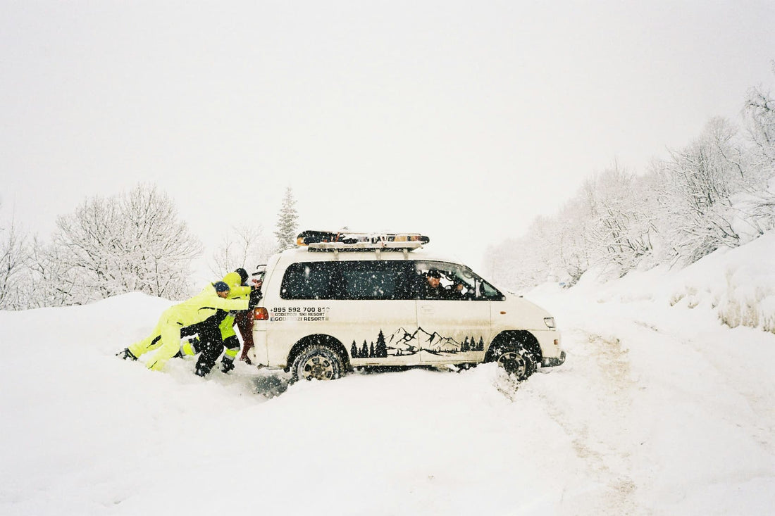 Ludzie pchaja vana zakopanego w glebokim sniegu na zimowej, zasniezonej drodze.