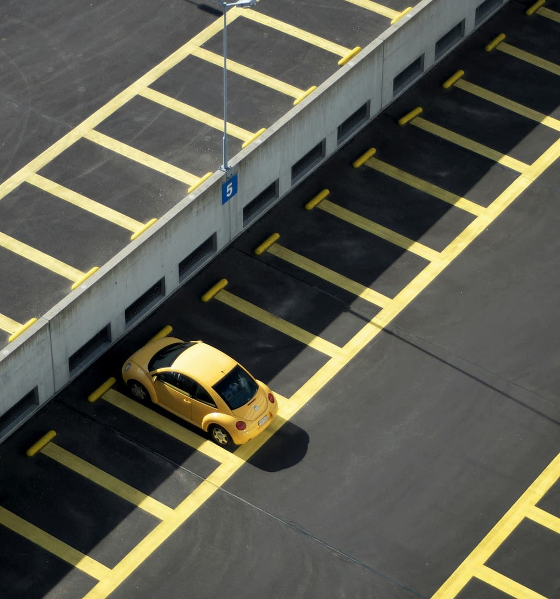 Żółty samochód kompaktowy zaparkowany samotnie na pustym oznakowanym parkingu.