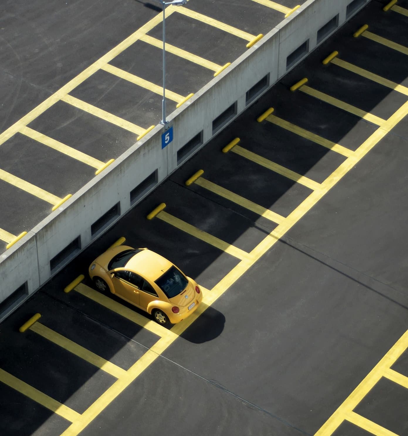 Żółty samochód kompaktowy zaparkowany samotnie na pustym oznakowanym parkingu.